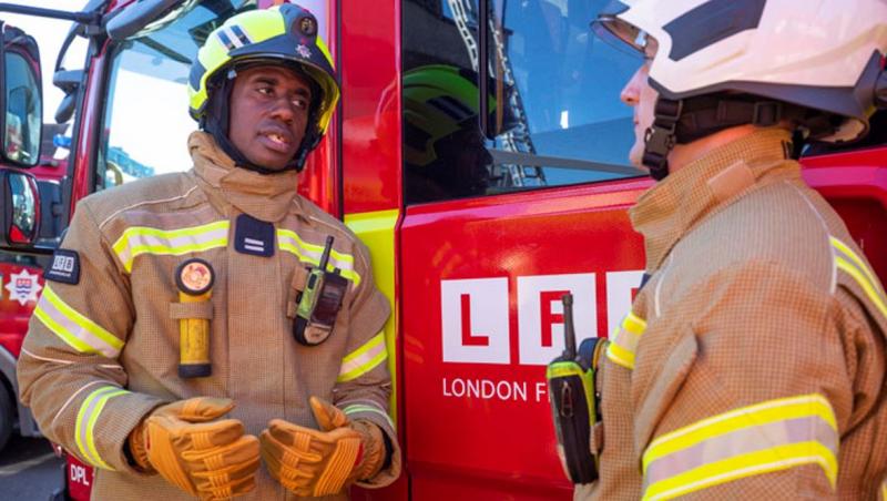 two firefighters in uniform and helmets outdoors infront of fire truck